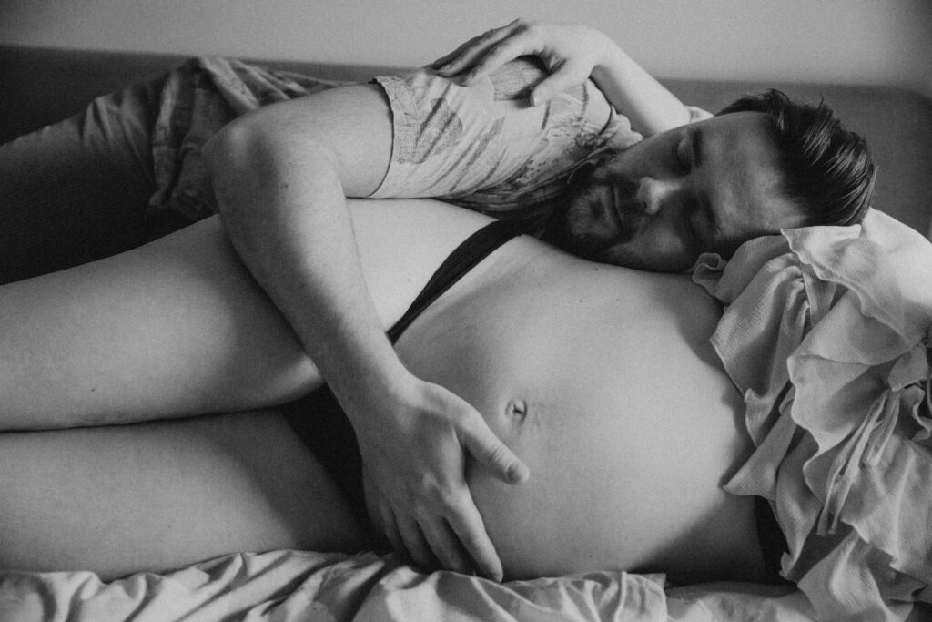 odotuskuvaus kotona makuuhuoneessa luonnonvalossa missä mies halaa raskausmahaa