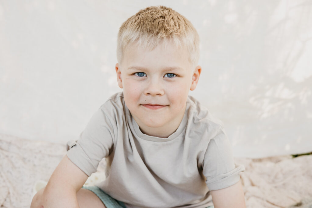 poika katsoo kameraan ja hymyilee perhekuvassa