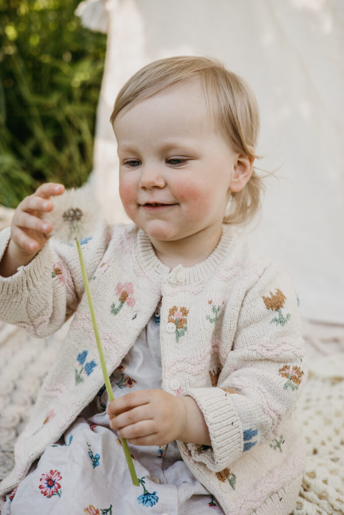 tyttö katsoo voikukkaa ja hymyilee miljöössä