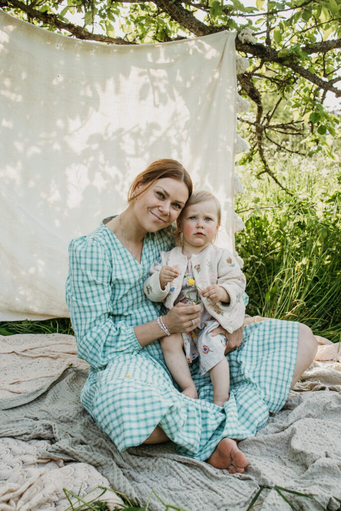 Äiti pitää taaperoa sylissä, miljöössä katse kameraan päin