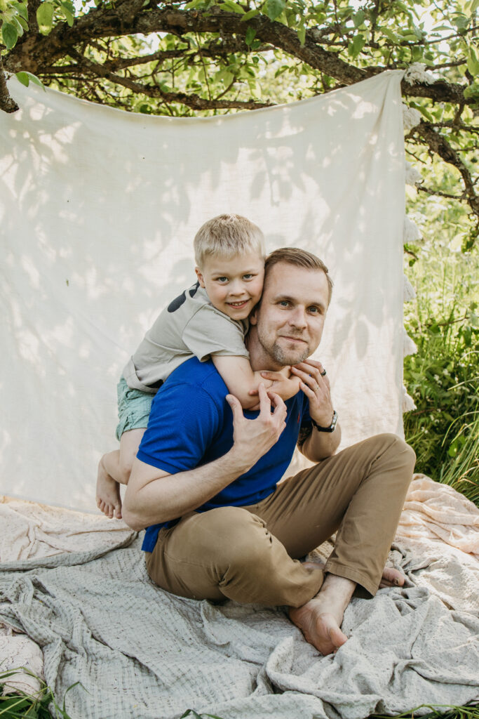 isä ja poika  istuvat viltillä puutarhassa ja tutkivat kukkia – lämmin ja luonnollinen perhekuvaus ulkona