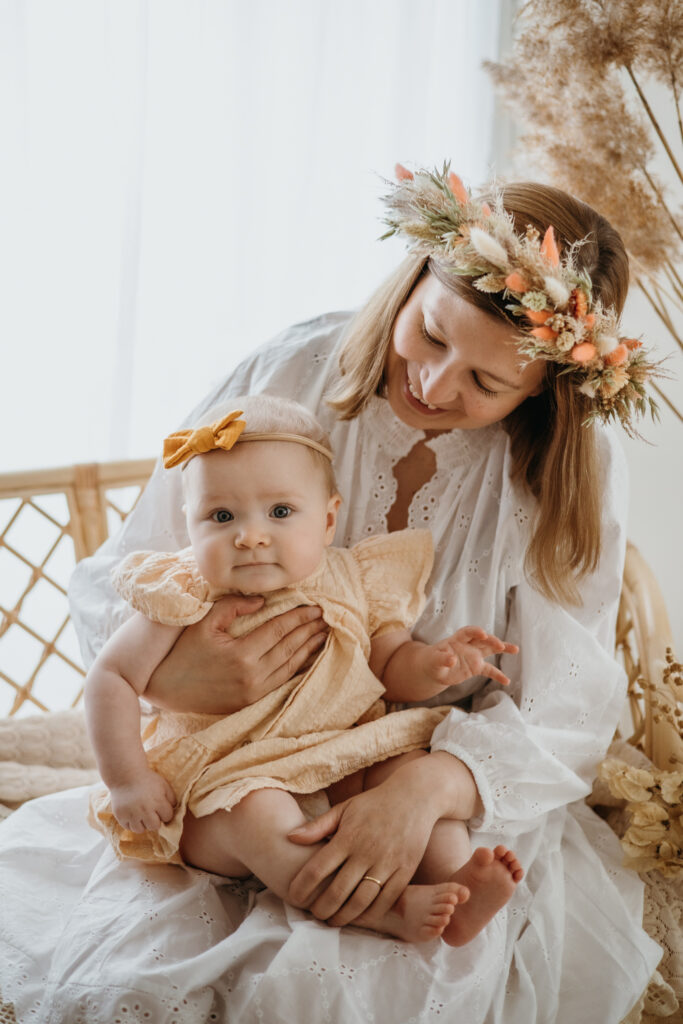 vauvakuvaus jossa äiti kastoo vauvaan kukkaseppele päässä