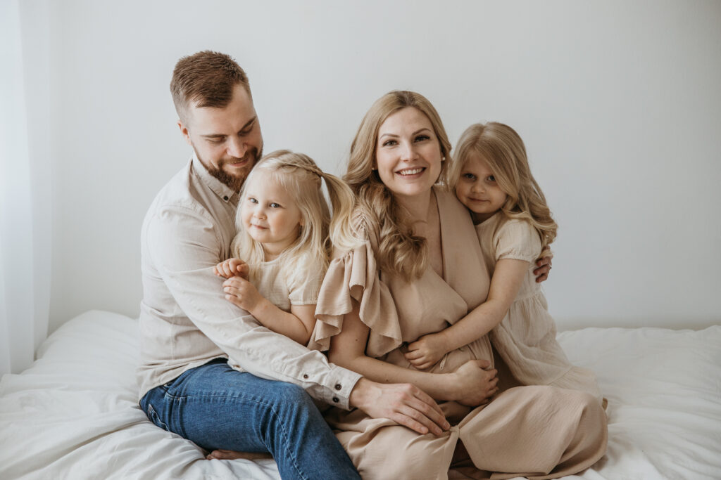 Odottava äiti, puoliso sekä ja lapsi halaavat raskausvatsaa – perhekuvaus studiossa