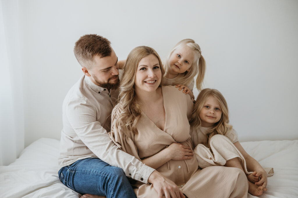 Odottava äiti ja lapsi halaavat raskausvatsaa – perhekuvaus studiossa