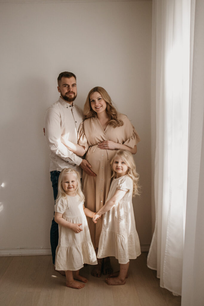 Odottava äiti ja puoliso sekä lapset vaaleassa studiossa – raskauskuvaus luonnonvalossa