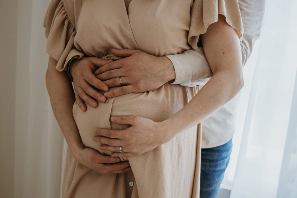 lähikuva käsistä ja raskausmaha