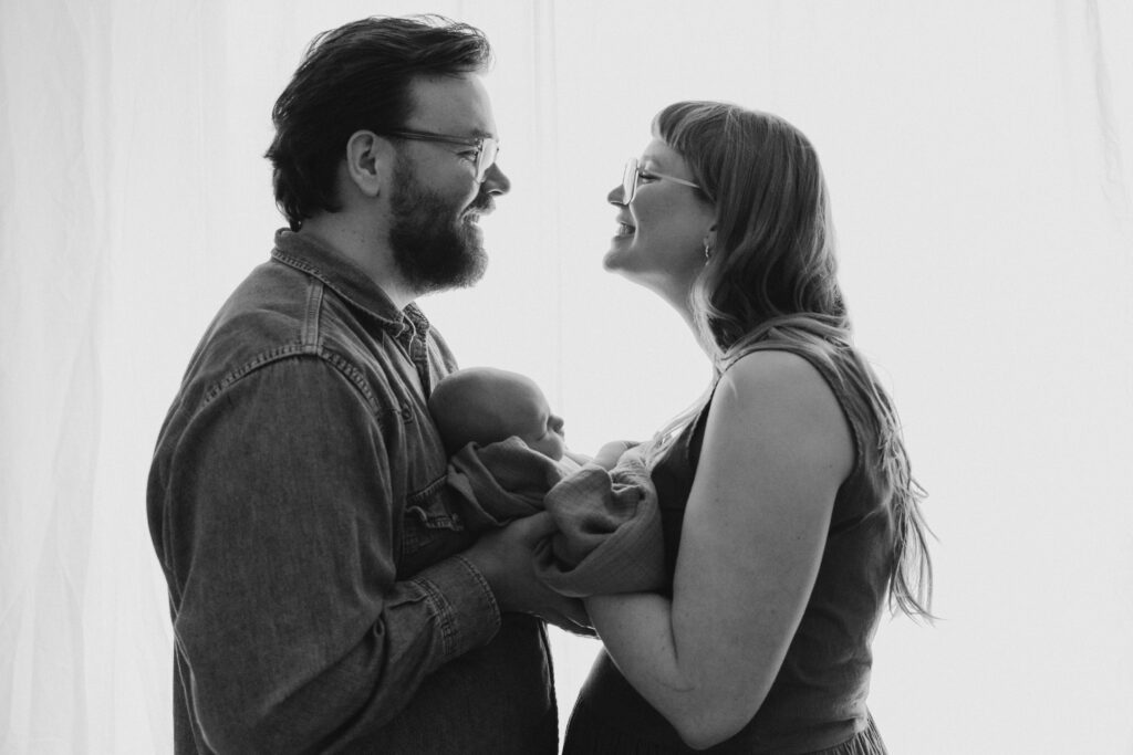 vastasyntynyt vauva vanhempien sylissä kuvattuna ikkunaa vasten