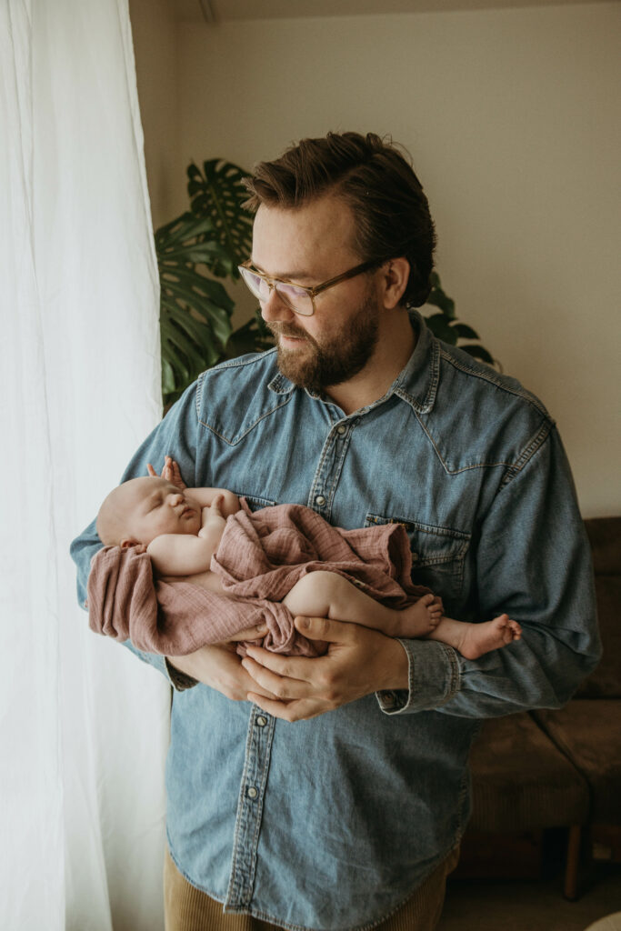 isä ja vastasyntynyt vauva kuvattuna ikkunan edessä- newbornkuvaus Helsinki