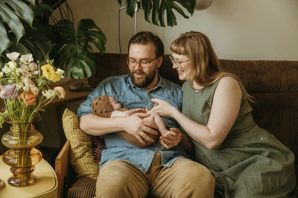 Vanhemmat hymyilevät ja ovat vastasyntyneen vauvan kanssa sohvalla